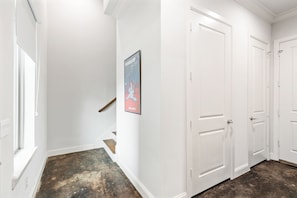 Un couloir aux murs blancs, un escalier et une affiche. Il y a trois portes blanches sur le côté droit.