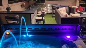 Un bain à remous avec éclairage bleu, des sièges extérieurs et une vue sur la ville la nuit.
