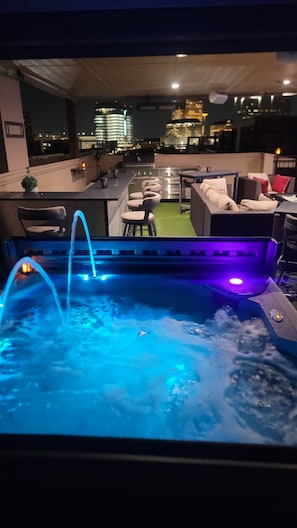 Un bain à remous avec éclairage bleu, des sièges extérieurs et une vue sur la ville la nuit.