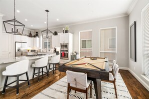 A modern kitchen with white cabinetry, a central island, and a pool table.