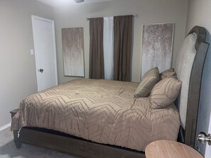 Ein Schlafzimmer mit Bett, Vorhängen, einer Tür und einem an der Wand befestigten Kunstwerk.