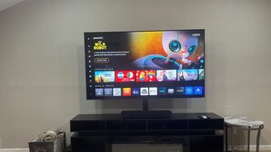 Ein Flachbildfernseher ist an einer schwarzen Unterhaltungseinheit befestigt, daneben steht ein Tisch mit Marmorplatte.