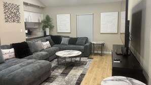Ein Wohnzimmer mit einem Ecksofa, einem runden Couchtisch, einem Fernseher und Kunstwerken an den Wänden.