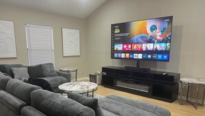 Ein modernes Wohnzimmer mit grauem Sofa, Couchtisch, flachbildfernseher an der Wand und schwarzem Unterhaltungsschrank darunter.