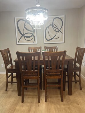 Een eetruimte met een houten tafel en stoelen, een kroonluchter en abstracte kunst aan de muur.