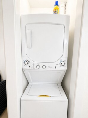 A white washing machine with control knobs and a detergent bottle on top. - Bellevue Escape In Downtown Dallas (Dallas)