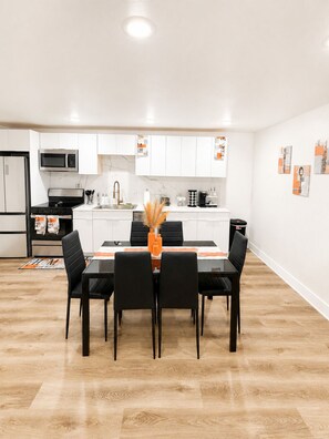 A modern kitchen with white cabinets, a microwave, stove, and a dining area with a table and chairs. - Bellevue Escape In Downtown Dallas (Dallas)