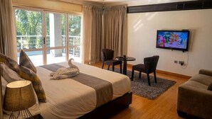 Una habitación de hotel con una cama, televisión, balcón, una mesita pequeña y un sofá.