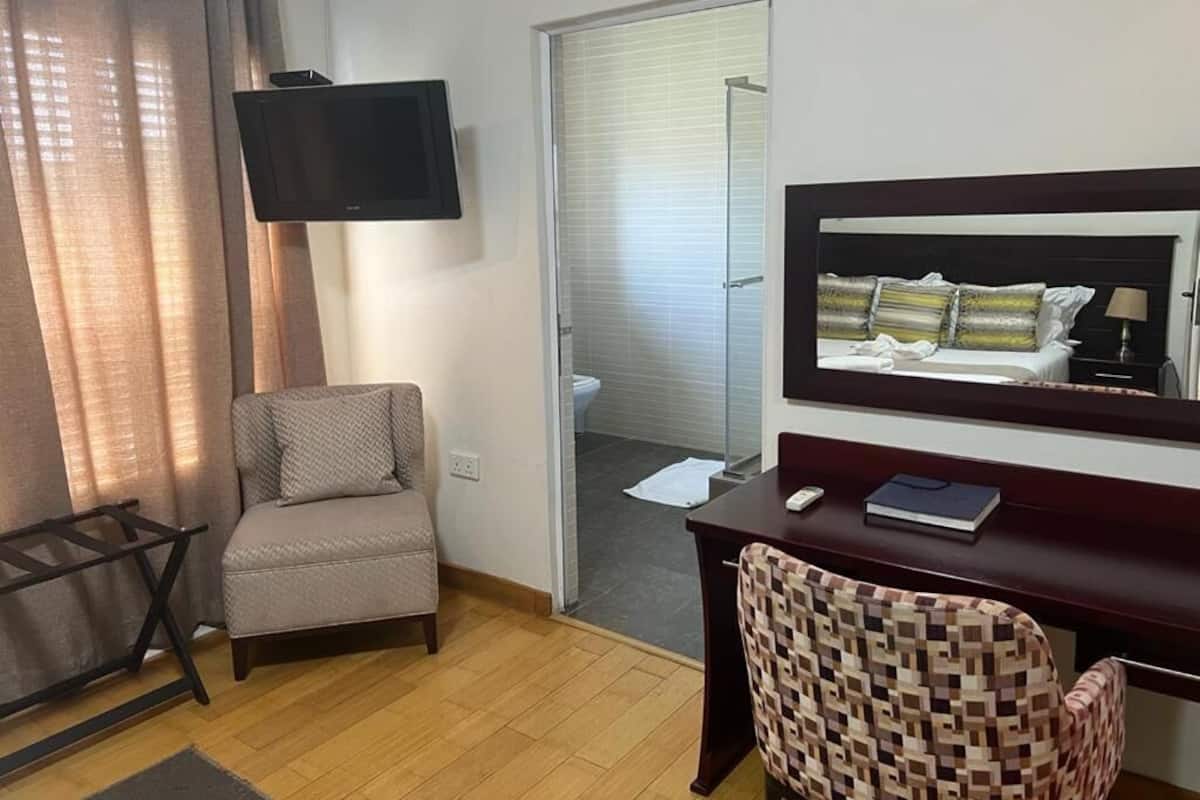 A hotel room with a TV, a desk with a chair, a bed with a headboard, and a bathroom visible through a door.