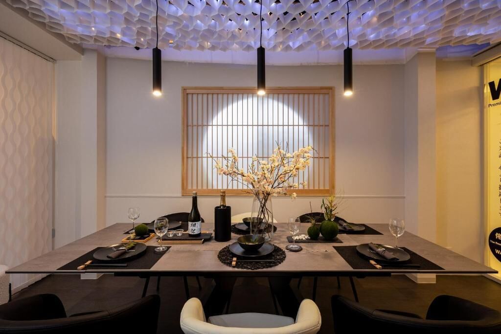 A dining area with a modern table set for four, a vase of flowers, and a bottle of wine.