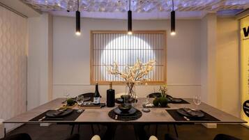 A dining area with a modern table set for four, a vase of flowers, and a bottle of wine.