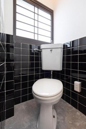 A toilet in a bathroom with black tiled walls and a window above it. - JAPAVISTA Wabi (Higashimikuni)