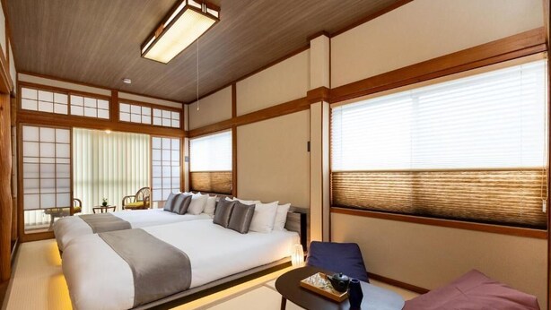 Ett traditionellt japanskt rum med tatamimattor på golvet, en stor säng med många kuddar, ett litet bord med ett bricka och skjutdörrar.