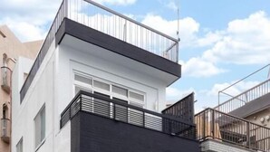 En modern byggnad i två våningar med en svartvit fasad, en balkong på övervåningen och en liten träbänk utanför.