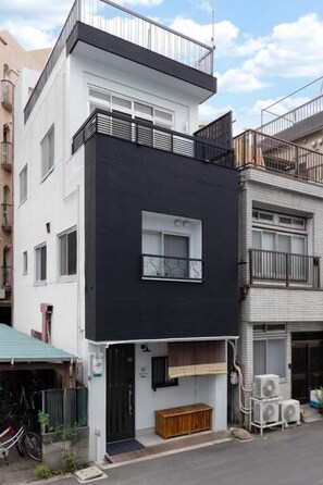 A modern two-story building with a black and white facade, a balcony on the upper floor, and a small wooden bench outside. - JAPAVISTA Wabi (Higashimikuni)