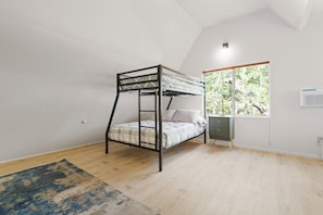 Ein Zimmer mit einem Etagenbett, einem Fenster mit Blick auf Bäume, einem kleinen Schrank und einem Holzboden.