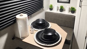 Una kitchenette compacta con una encimera, dos platos negros, un rollo de toallas de papel, un salero y un cuadro con cubiertos.