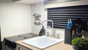 Una kitchenette compacta con microondas, lavamanos y un adhesivo de pared con motivos de café.