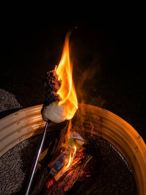 Ein Lagerfeuer mit einem Marshmallow am Spieß, umgeben von einem Metall-Feuerkorb.