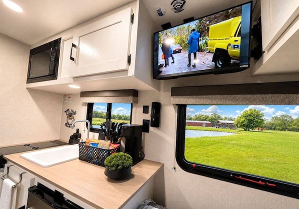 A kitchen with a sink, countertop, and a television mounted above it.