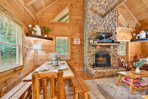 Ein Holzhäuschen im Inneren mit Kamin aus Stein, einem Holzesstisch, Bänken und einem Fernseher.