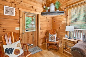 Ein Holzblockhaus-Interieur mit einer Tür, einem Sessel, einem kleinen Tisch und einer Couch.