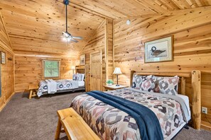 A wooden cabin room with two beds, a ceiling fan, a framed picture, and a window with blinds. - Linden Lodge 7BR Sleeps 16 Hot Tub;Old Mans Cave (Logan)