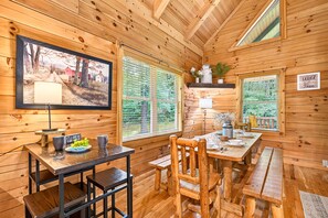 Ein Holzblockhaus-Innenraum mit Esstisch, Stühlen, einem Fernseher und einem Schild mit der Aufschrift 'Wild Free'.