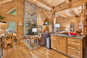 Ein rustikales Cabin-Interieur mit Kamin aus Stein, einem Essbereich aus Holz und einer Küchenzeile.
