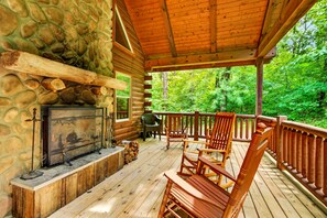 Eine Blockhütte mit Kamin aus Stein, einer Holzterrasse und Sitzgelegenheiten im Freien.