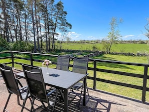 Eine Terrasse mit Tisch und Stühlen, mit Blick auf eine Wiese und Bäume.