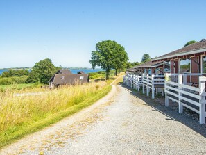 A gravel path leading to a building with a white fence, a tree, and a view of the sea. - 4 Person Holiday Home in Aabenraa (Aabenraa)