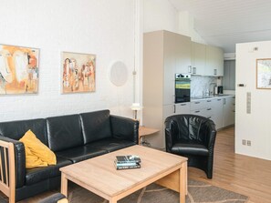 A modern living room with a black leather sofa, a wooden coffee table, and a black leather armchair. There are abstract paintings on the wall and a kitchen in the background. - 4 Person Holiday Home in Aabenraa (Aabenraa)
