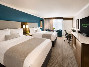 A hotel room with two beds, a desk, a chair, a television, and a window with curtains.