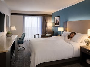 A hotel room with a bed, desk, chair, lamps, and a cityscape picture on the wall. - Comfortable hotel suites in enchanting Oklahoma City with fitness room, pool. (Oklahoma City)