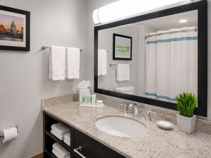 A hotel bathroom with a large mirror, a sink, a toilet, and a framed picture of a cityscape.