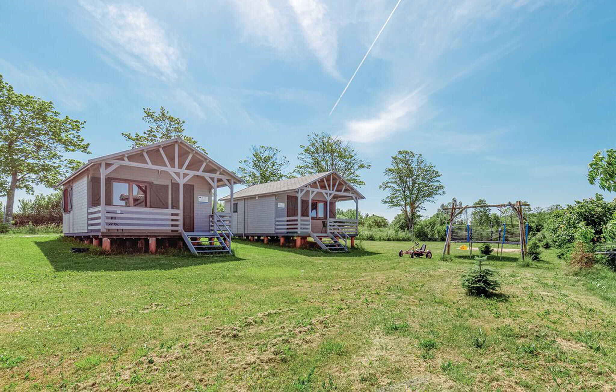 Two small wooden cabins with porches, set in a grassy area with trees and a clear sky.