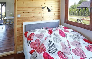A bedroom with a wooden wall, a bedside lamp, a bed with a patterned blanket, and a view of the outdoors. - Stunning home in Mscice (Mscice)