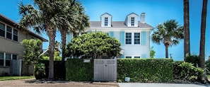 A two-story house with a gated entrance, surrounded by palm trees and a hedge. - Bayfront Breeze on Ocean Drive Sleeps 15 (Corpus Christi)