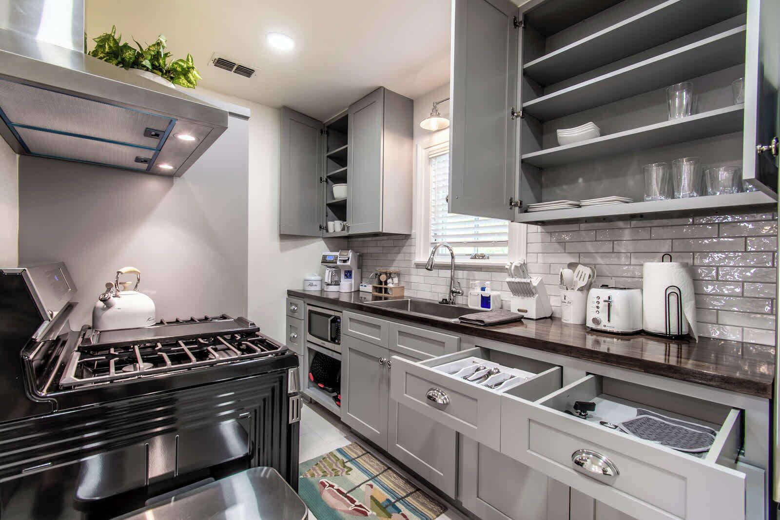 A modern kitchen with a gas stove, microwave, and built-in oven. There are grey cabinets, a sink, and a window with blinds.