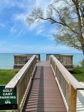 Ein Holzsteg führt zu einem Strand, wobei ein Schild Golfwagenparkplätze kennzeichnet.
