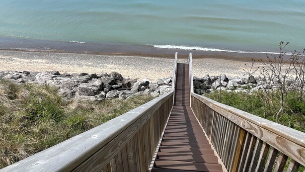 A wooden boardwalk leading to a beach with a view of the ocean.