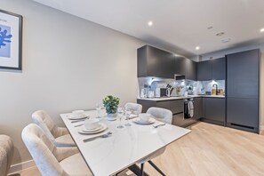 Een moderne keuken met donkere kastjes, een wit aanrechtblad en een eethoek met een witte tafel voor vier personen.