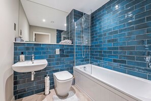 Een moderne badkamer met een wit wastafel, toilet en bad, omringd door blauwe wandtegels.