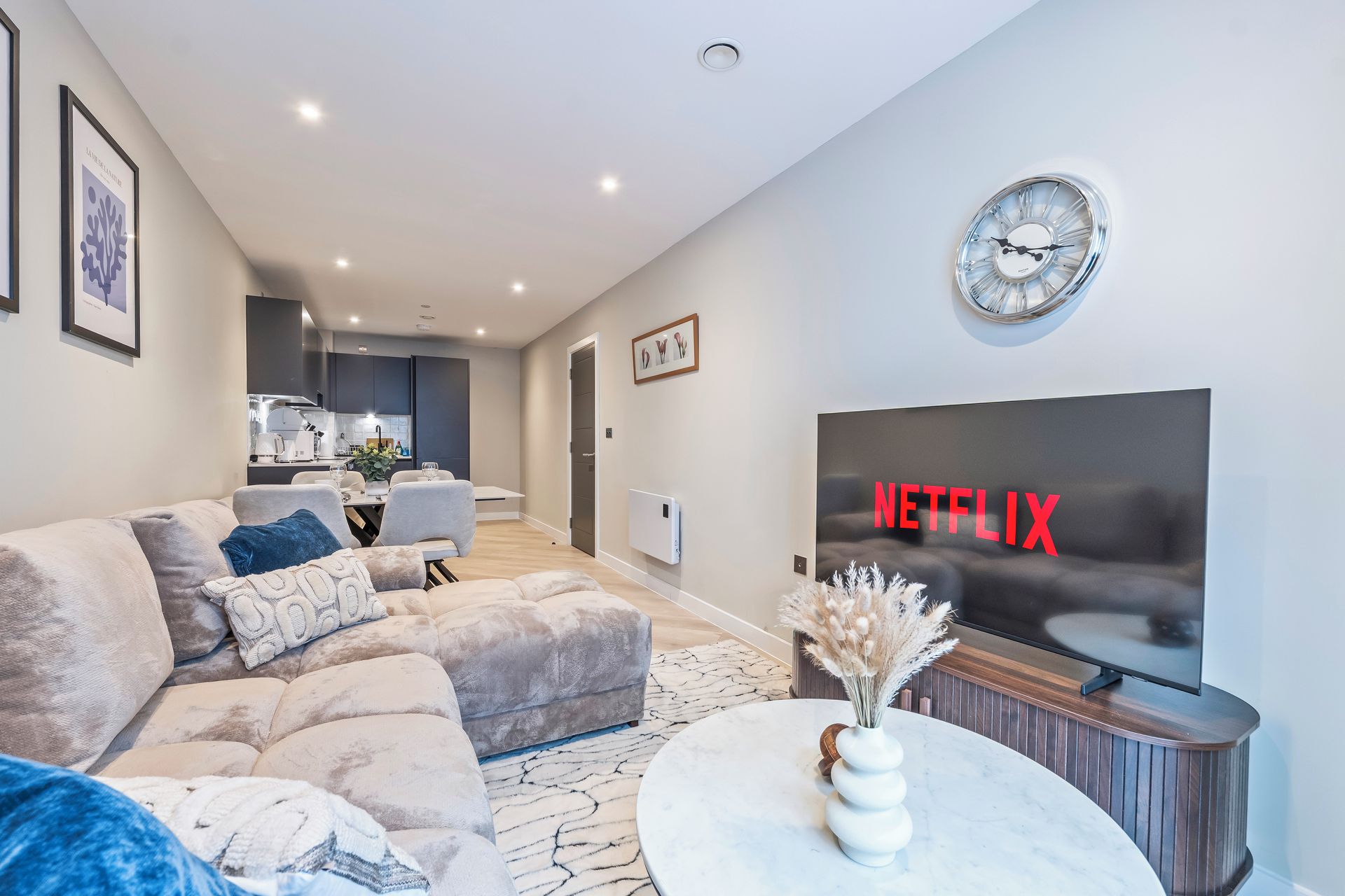 Un salon moderne avec un canapé, une table basse, une horloge murale et un grand écran de télévision affichant le logo de Netflix.