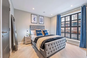 Ein Schlafzimmer mit einem großen Bett, einem Nachttisch, einer Kommode und einem Fenster mit Vorhängen.