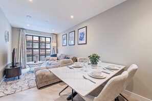 Un espace repas moderne avec une table dressée pour quatre personnes, un canapé et une grande fenêtre avec des rideaux.