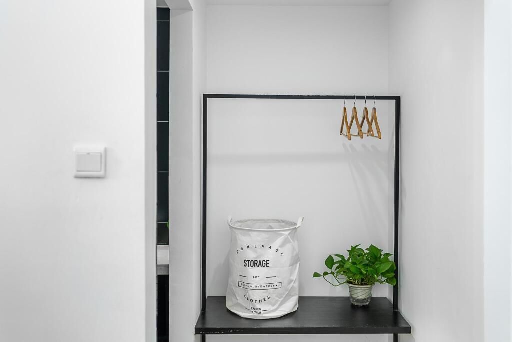 A white wall with a black-framed mirror, a white storage bag labeled 'STORAGE,' and a potted plant on a black shelf.