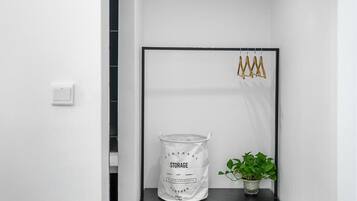 A white wall with a black-framed mirror, a white storage bag labeled 'STORAGE,' and a potted plant on a black shelf.