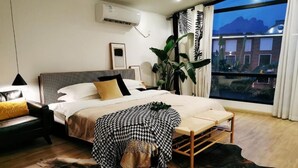 A bedroom with a bed, bedside table, lamp, and a view of the outside.